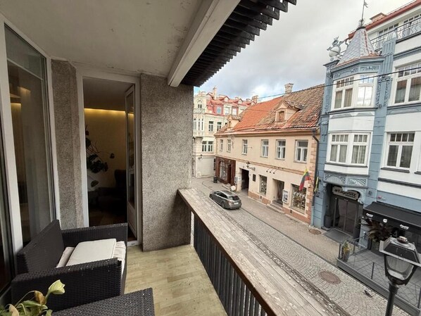 A balcony with wicker furniture, a view of a cobblestone street, and traditional European buildings.