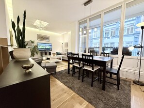 A modern living room with a dining area, large windows, and a television.