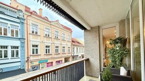 A balcony with wicker furniture, a potted plant, and a view of colorful buildings.