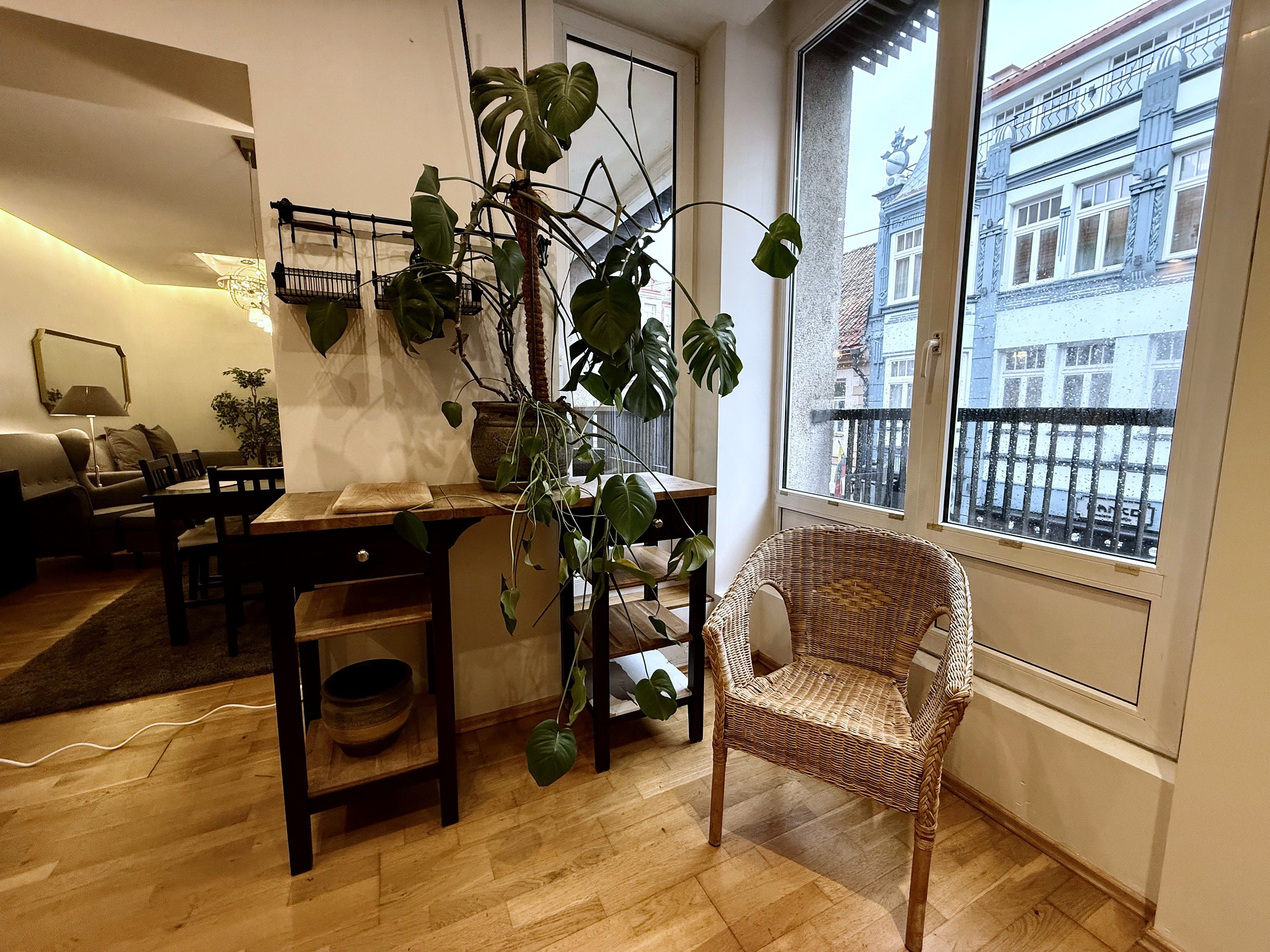 A cozy living room with a dining area, a wicker chair, and a large window with a view of a building.
