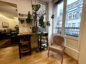 A cozy living room with a dining area, a wicker chair, and a large window with a view of a building.