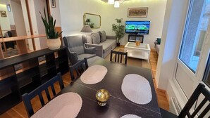 A modern living room with a dining area, a sofa, a TV, and a large window.