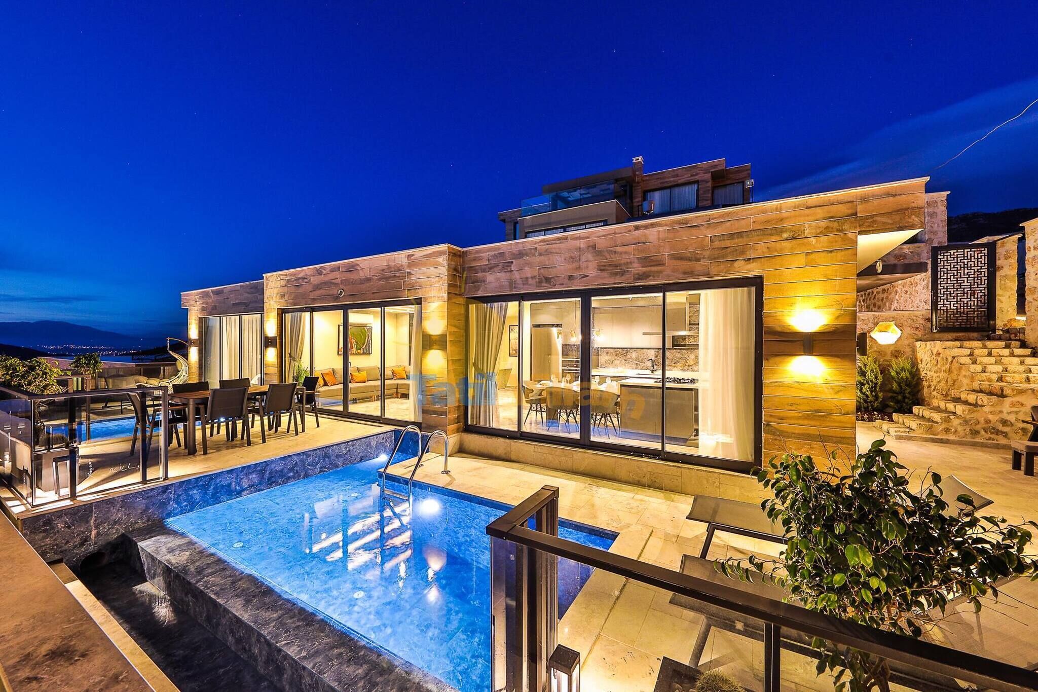 Une maison moderne dotée d’une piscine, d’un espace salon extérieur et de grandes fenêtres.