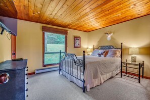 Ein Schlafzimmer mit Holzboden, einem Bett mit Dekoration im Hirschgeweih-Stil, einem Fenster mit Blick auf Grünflächen und einem Nachttisch mit Lampe.