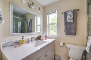 Ein Badezimmer mit weißem Waschtisch, einem großen Spiegel, einer Toilette und einem Fenster.