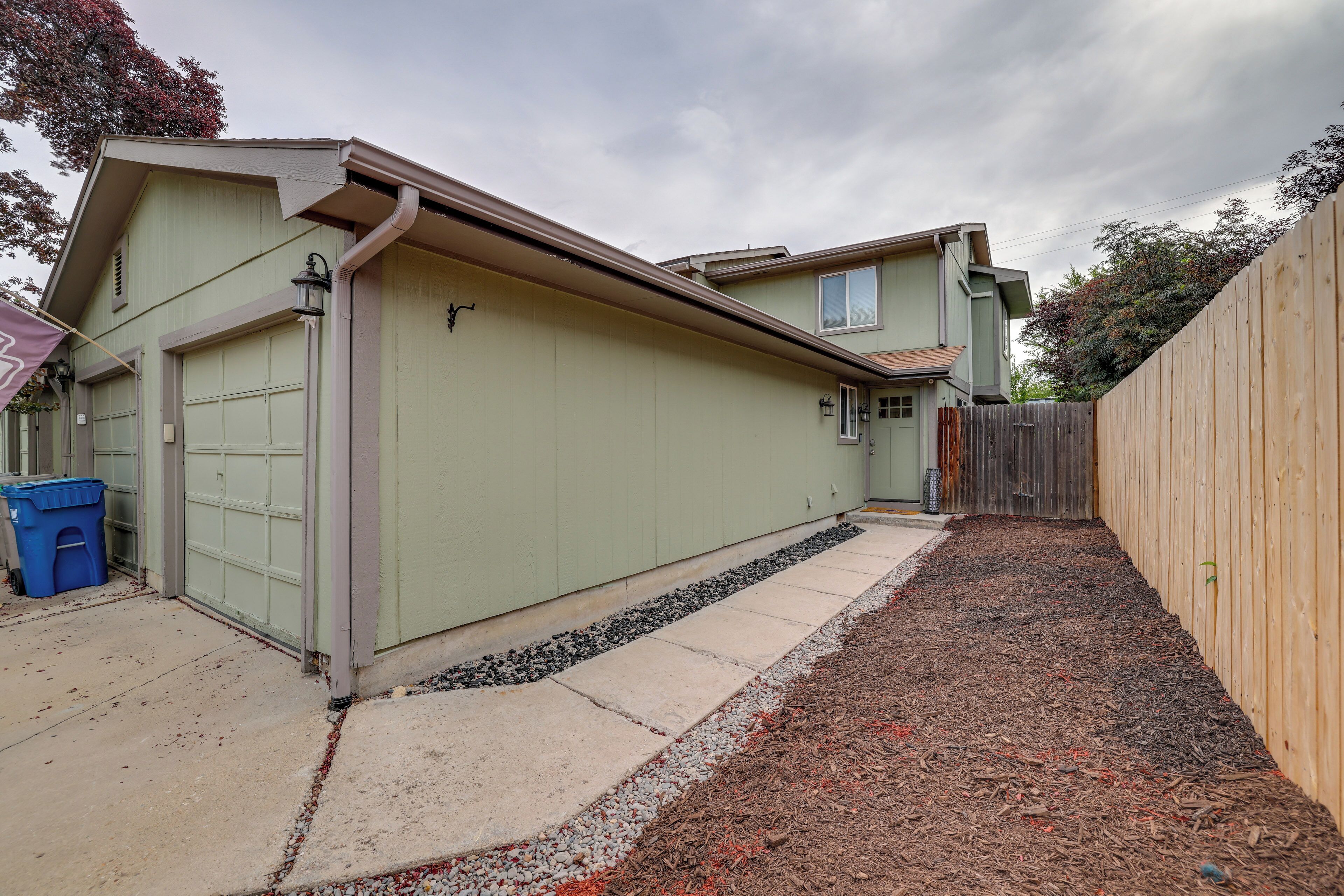A two-story house with a garage, a wooden fence, and a gravel driveway.