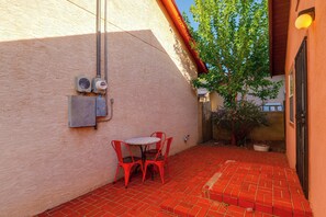 A patio with red brick flooring, a small round table with four red chairs, and a wall-mounted electrical box. - Couple’s Casita Near Historic Downtown Roswell! (Roswell)