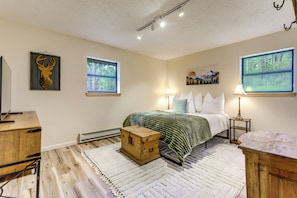 Ein Schlafzimmer mit einem Bett, zwei Fenstern, einem Wandbild eines Hirschkopfes, einem Gemälde und einer Holzkiste.