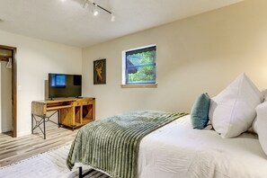 Une chambre à coucher avec un lit, un bureau avec une télévision, une fenêtre donnant sur un paysage agréable et une porte.
