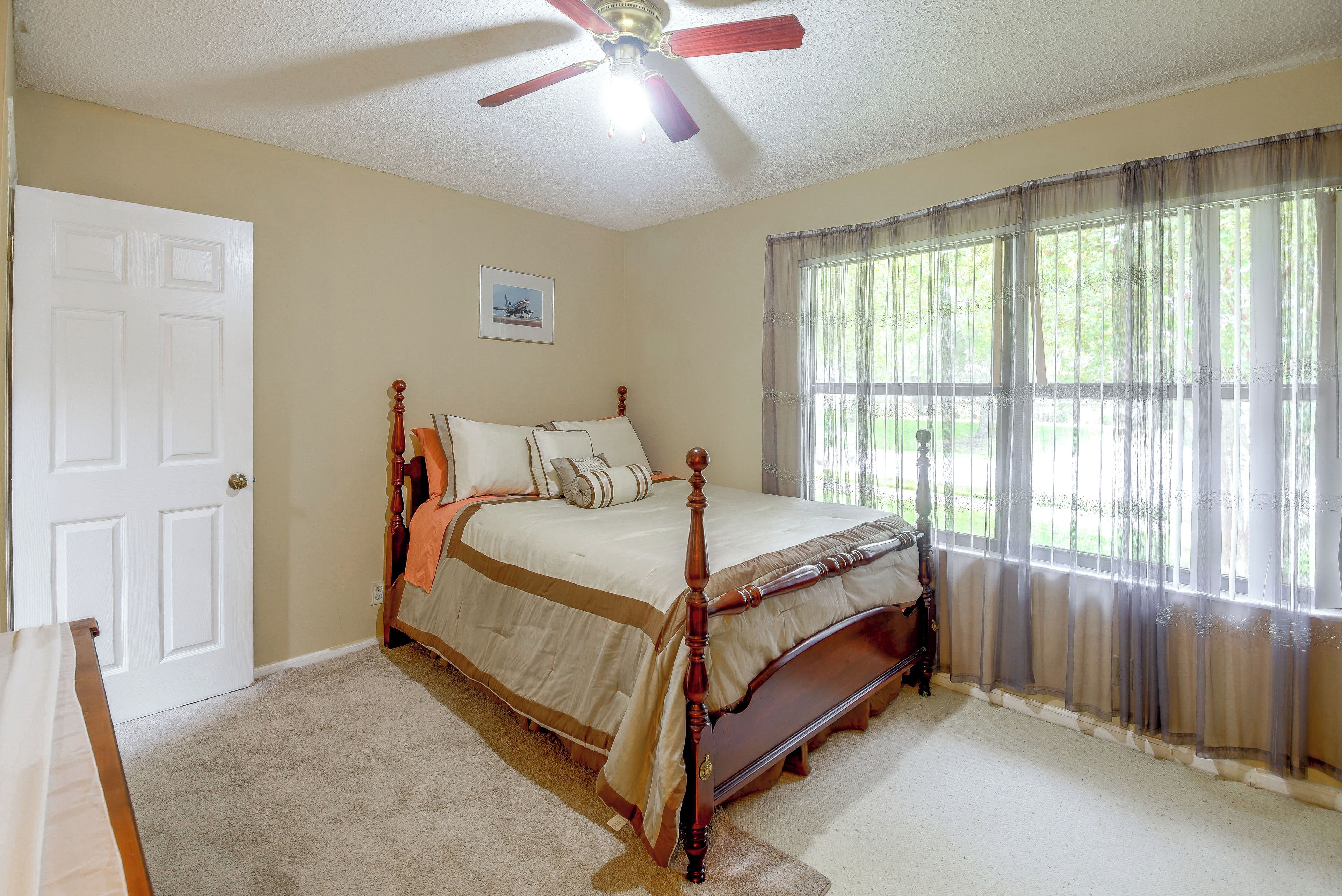 Une chambre à coucher avec un lit à baldaquin, un ventilateur de plafond, une fenêtre avec des rideaux légers et une porte.