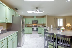 A kitchen with green cabinets, a refrigerator, a microwave, and a stove. There is a ceiling fan and a window with curtains. - Golf, Beach, Parks! Palm Coast Family Home w/ Yard (Palm Coast)