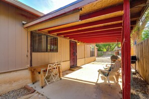A covered patio area with a wooden table and chairs, a red door, and a view of the backyard.