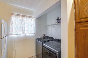 A compact kitchen with a refrigerator, stove, and a window with floral curtains.