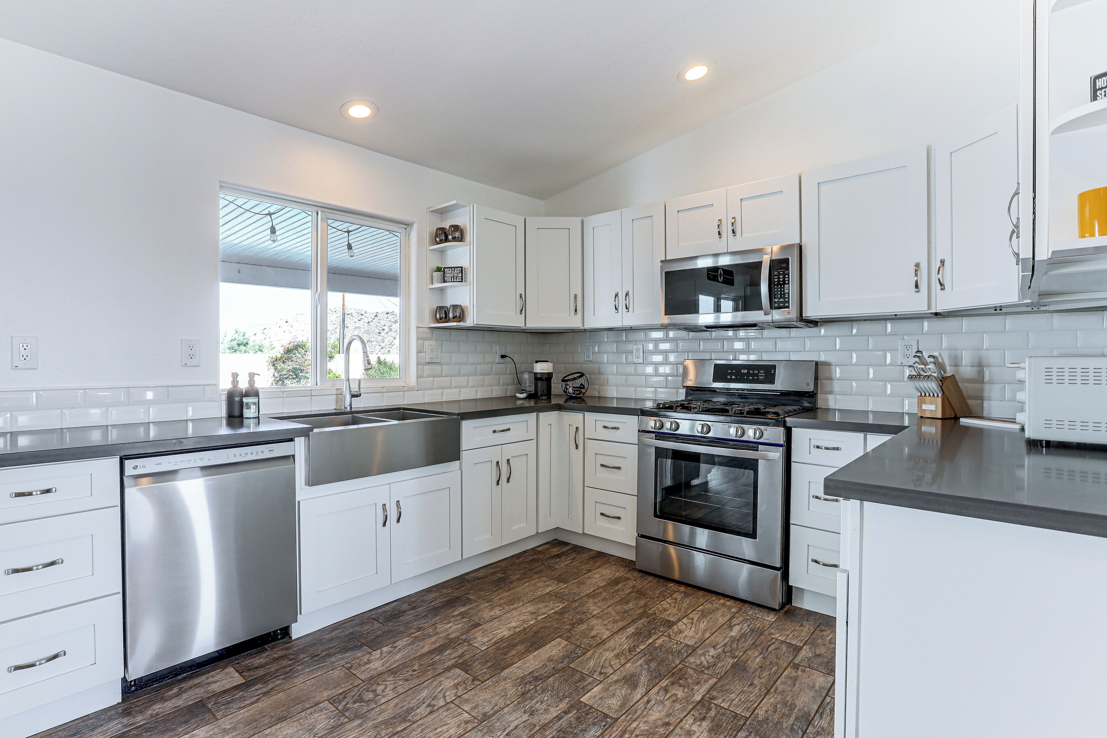 A modern kitchen with white cabinets, stainless steel appliances, and a wooden floor.