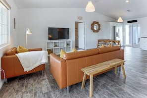 A modern living room with a sofa, a TV, and a wooden bench. - Heated Pool, Spa & Game Room: Yucca Valley Retreat (Yucca Valley)
