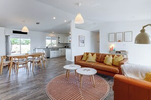 Ein modernes Wohnzimmer mit einem braunen Ledersofa, einem Esstisch mit Stühlen und einer Küche im Hintergrund.