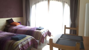 A hotel room with two beds, a table, and a chair.