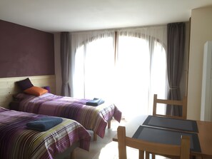 A hotel room with two beds, a table, and a chair.