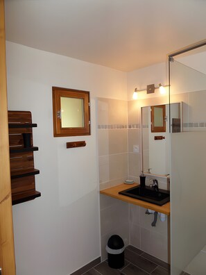 A bathroom with a wooden bench, a mirror, a sink, and a trash bin.