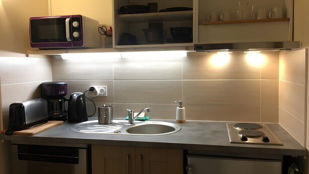 A compact kitchen with a microwave, coffee maker, sink, and a stove.