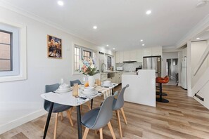 A modern kitchen with white cabinets, a stainless steel refrigerator, and a dining area with a white table and grey chairs. - Charming Character Terrace, Eclectic Vintage Charm (Petersham)