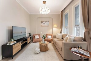 A modern living room with a flat-screen TV, a sofa set, a coffee table, and a decorative plant. - Charming Character Terrace, Eclectic Vintage Charm (Petersham)