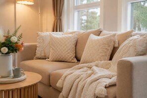 A beige sofa with patterned cushions, a throw blanket, and a vase with flowers on a wooden side table.