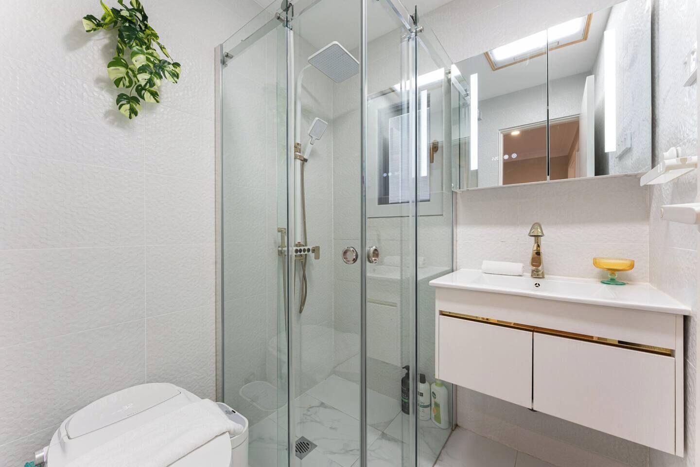 A modern bathroom with a glass-enclosed shower, a white sink with gold trim, and a mirror above the sink.