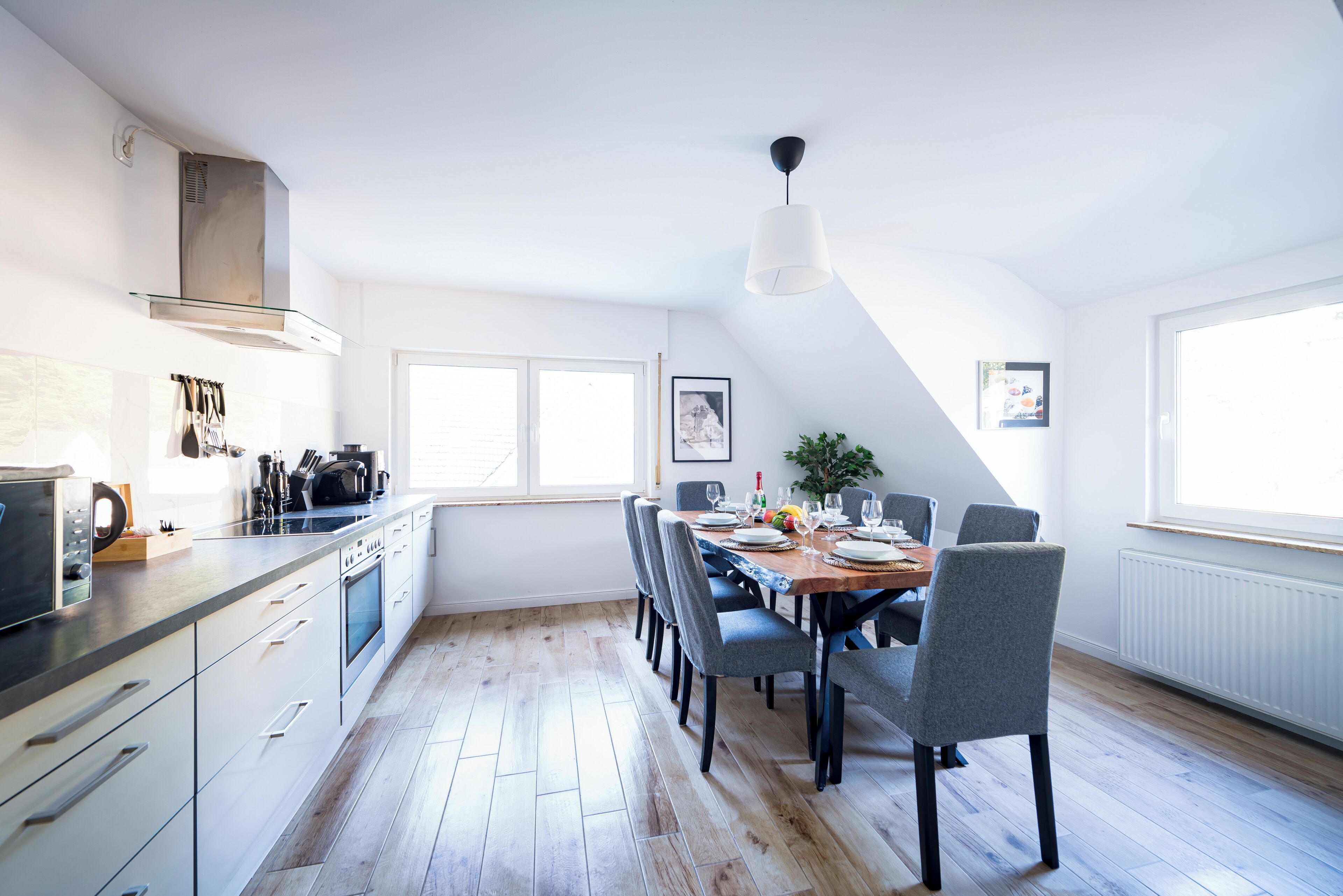 A modern kitchen with a dining area, wooden flooring, and a view of the outdoors.