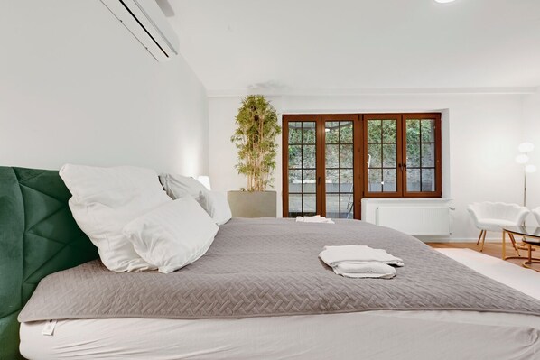 Un dormitorio moderno con una cama grande, una planta en maceta y vistas al exterior a través de una puerta corrediza de vidrio.