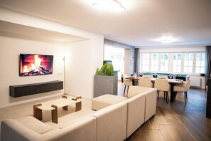 Una sala de estar moderna con televisor de pantalla plana, chimenea, comedor con mesa y sillas, y un ventanal con vistas.