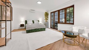 Un dormitorio moderno con cama, mesitas de noche, un escritorio, una silla y un ventanal grande.