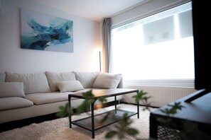 Un salon moderne avec un canapé, une table basse et une grande fenêtre agrémentée de rideaux.