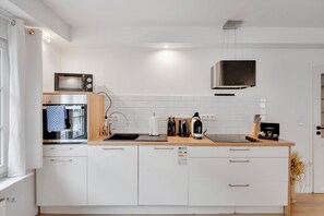 Una cocina moderna con armarios blancos, un microondas, una tetera y una cafetera sobre la encimera.