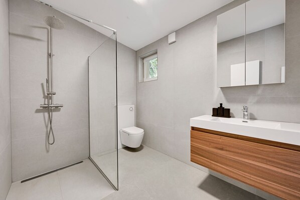 Un baño moderno con cabina de ducha de vidrio, inodoro blanco y tocador de madera con espejo.
