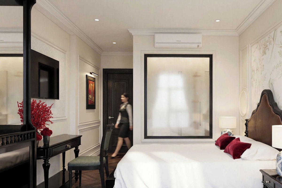 Een hotelkamer met een bed, nachtkastje, lamp en een groot raam.