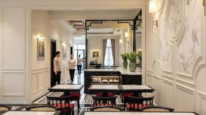 Een hotel lobby met een receptiebalie, een zithoek met tafels en stoelen, en een trap naar een andere verdieping.