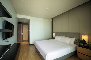 A hotel room with a bed, bedside tables, a TV mounted on the wall, and a door leading to another room. - Coast & Nest apartment (Đà Nẵng)