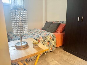 Een slaapkamer met een bed, nachtkastje, lamp en een kledingkast.