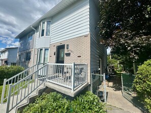 A two-story residential building with a front porch and a staircase leading to the entrance.