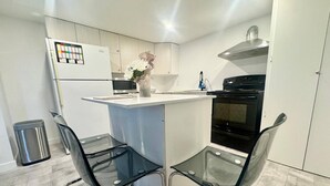 A modern kitchen with a central island, two glass chairs, a stainless steel trash bin, and a black stove.