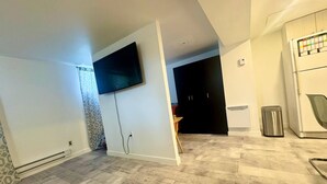 A modern living room with a flat-screen TV mounted on the wall, a kitchen area with a refrigerator, and a patterned wall.