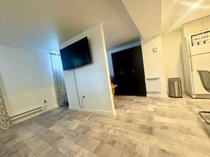 A modern living room with a flat-screen TV mounted on the wall, a kitchen area with a refrigerator, and a patterned wall.