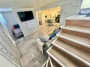 Een moderne woonkamer met een bank, een flatscreen-tv aan de muur en een trap naar een hoger niveau.