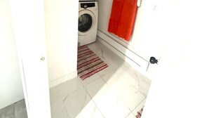 A laundry room with two stacked washing machines, a red towel hanging on a rack, and a striped rug on the floor.
