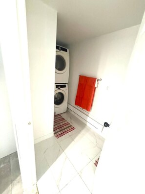A laundry room with two stacked washing machines, a red towel hanging on a rack, and a striped rug on the floor.