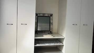 A white wardrobe with a mirror and shelves, a keyboard, and a laptop on the top shelf.