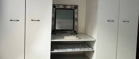 A white wardrobe with a mirror and shelves, a keyboard, and a laptop on the top shelf.