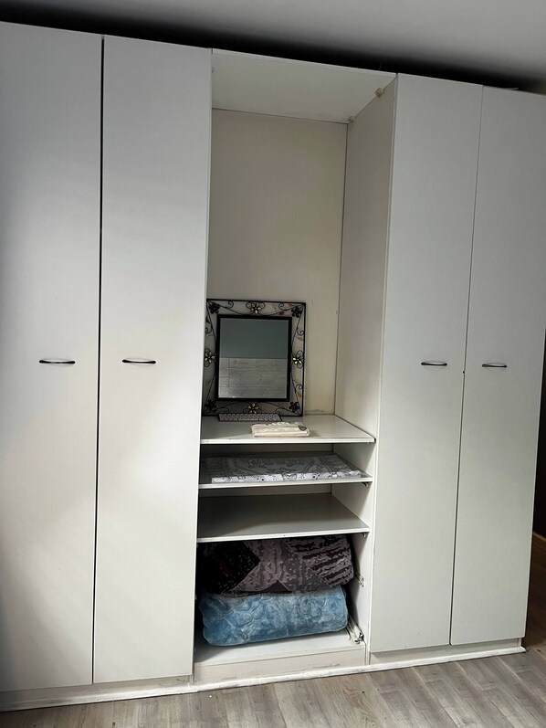 A white wardrobe with a mirror and shelves, a keyboard, and a laptop on the top shelf.