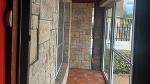 A corridor with stone walls and a tiled floor, leading to a glass door with a view of a garden. - Spacious House Rental with Private Rooms in Cape Town (Cape Town)